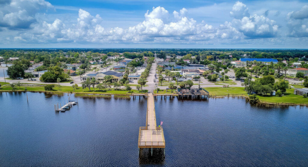Aerial view of Clermont, Florida, featuring a long wooden pier over Lake Minneola with the town and palm-lined streets in the background.