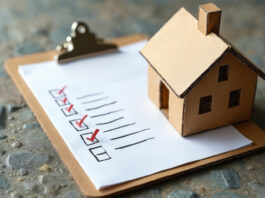 Clipboard checklist with miniature cardboard house on stone background. Moving checklist