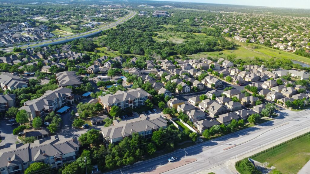 Aerial view of East Austin, Texas, featuring suburban homes and apartment complexes surrounded by lush greenery with a highway running through the area, illustrating the blend of residential living and access to nature.