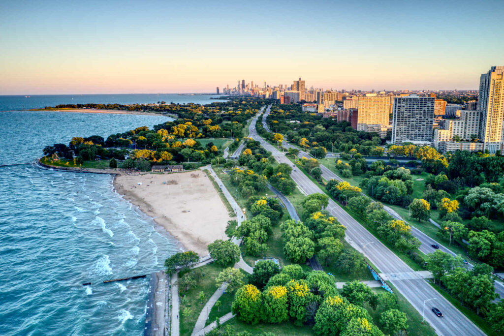 Aerial view of Edgewater, Chicago, featuring Lake Michigan’s shoreline, green spaces, and city skyline in the distance at sunset.