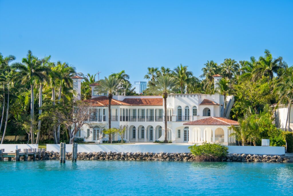 Luxury waterfront mansion in Miami with palm trees and clear blue water, reflecting the city’s high-end real estate market.