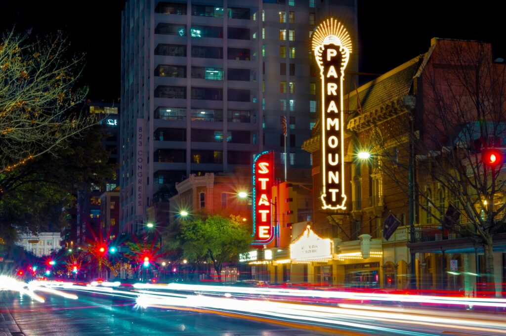 Night-time street view of downtown Austin, Texas, showcasing the vibrant lights of the Paramount and State theatres, reflecting the city's lively cultural scene and urban lifestyle.
