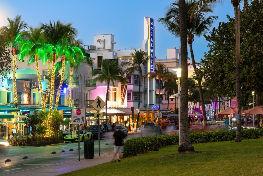 Evening view of Ocean Drive in Miami’s South Beach, with neon-lit Art Deco buildings, palm trees, and a lively street scene.