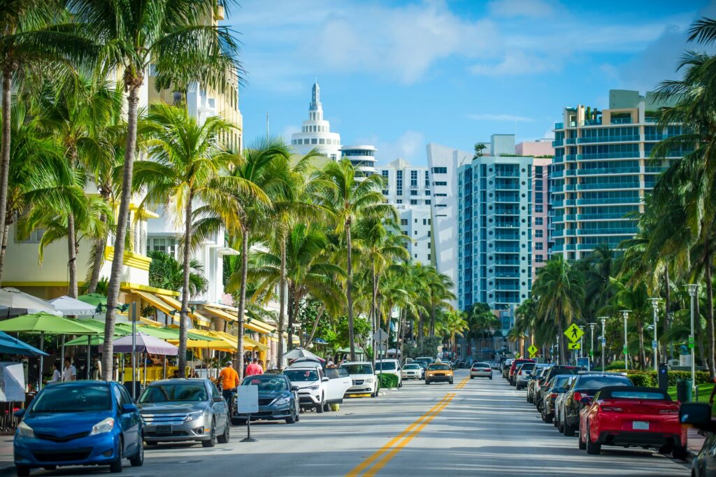Busy street in Miami lined with palm trees, parked cars, and colourful buildings, highlighting the city's car-centric transport and vibrant urban layout.