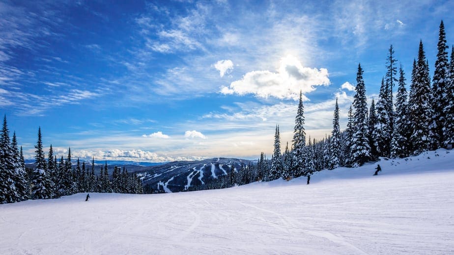 Skiing down smooth slopes under blue sky in the high alpine ski area at Sun Peaks in the Shuswap Highlands of central British Columbia, Canada