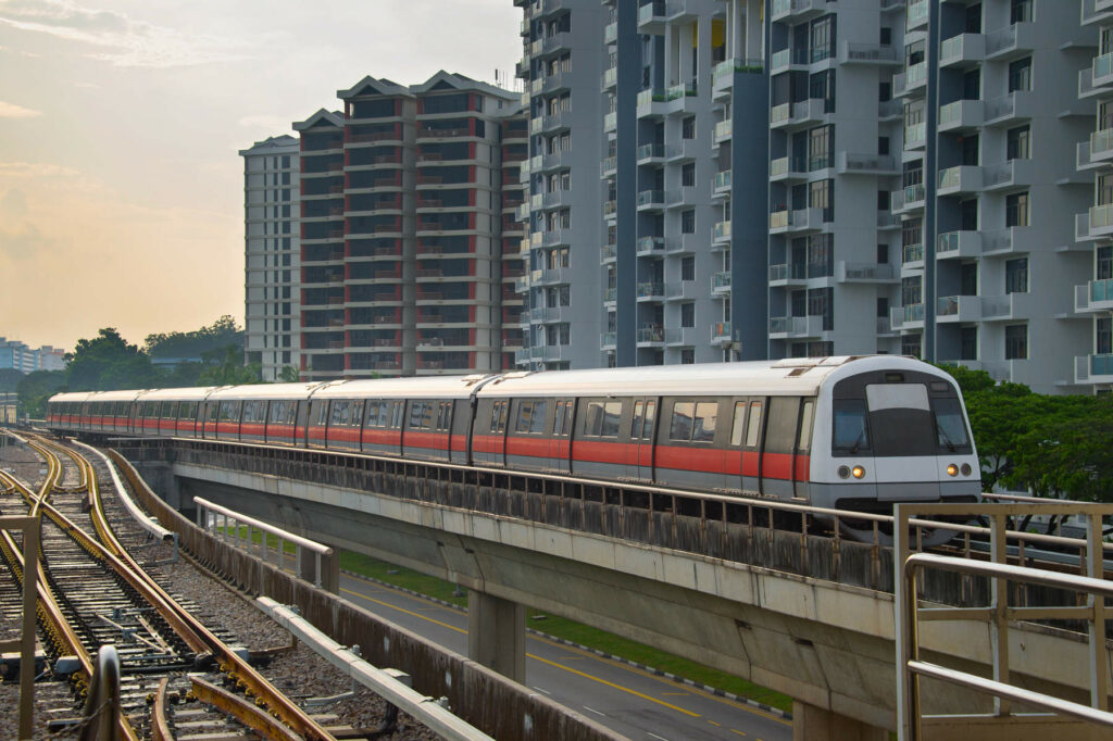 Singapore MRT train on an elevated track passing residential buildings, representing the city's efficient public transport system.