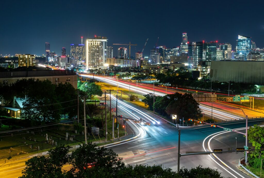 Nighttime view of downtown Austin with light trails from vehicles on the highway, highlighting the city's growth and transportation network.