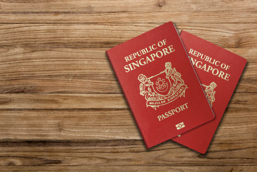 Two Singapore passports placed on a wooden surface, symbolising travel, citizenship, or visa requirements for moving to Singapore.